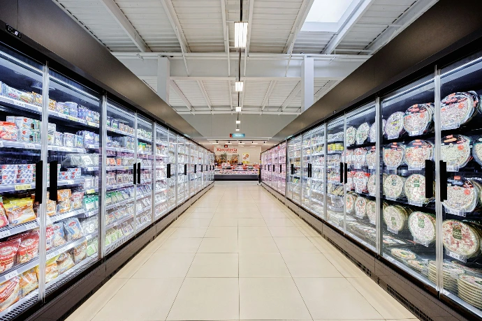 A long aisle in a brightly lit supermarket with refrigerators.